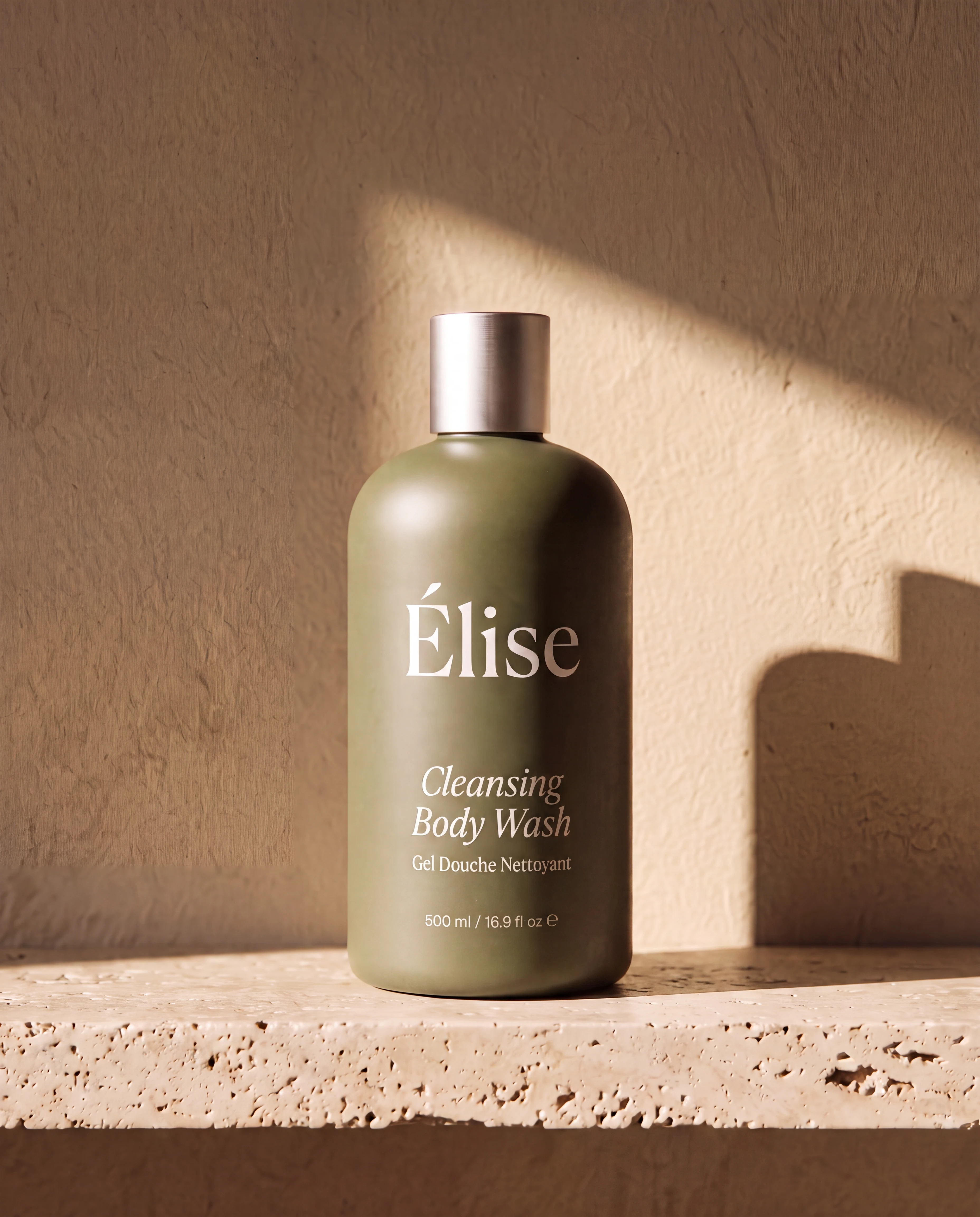 One olive Elise cleansing body-wash bottle grounded on a sunlit travertine shelf