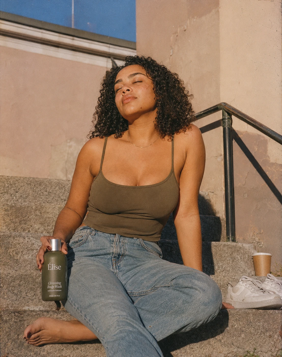 A woman seated in hard afternoon light with one Elise bottle held naturally at her side