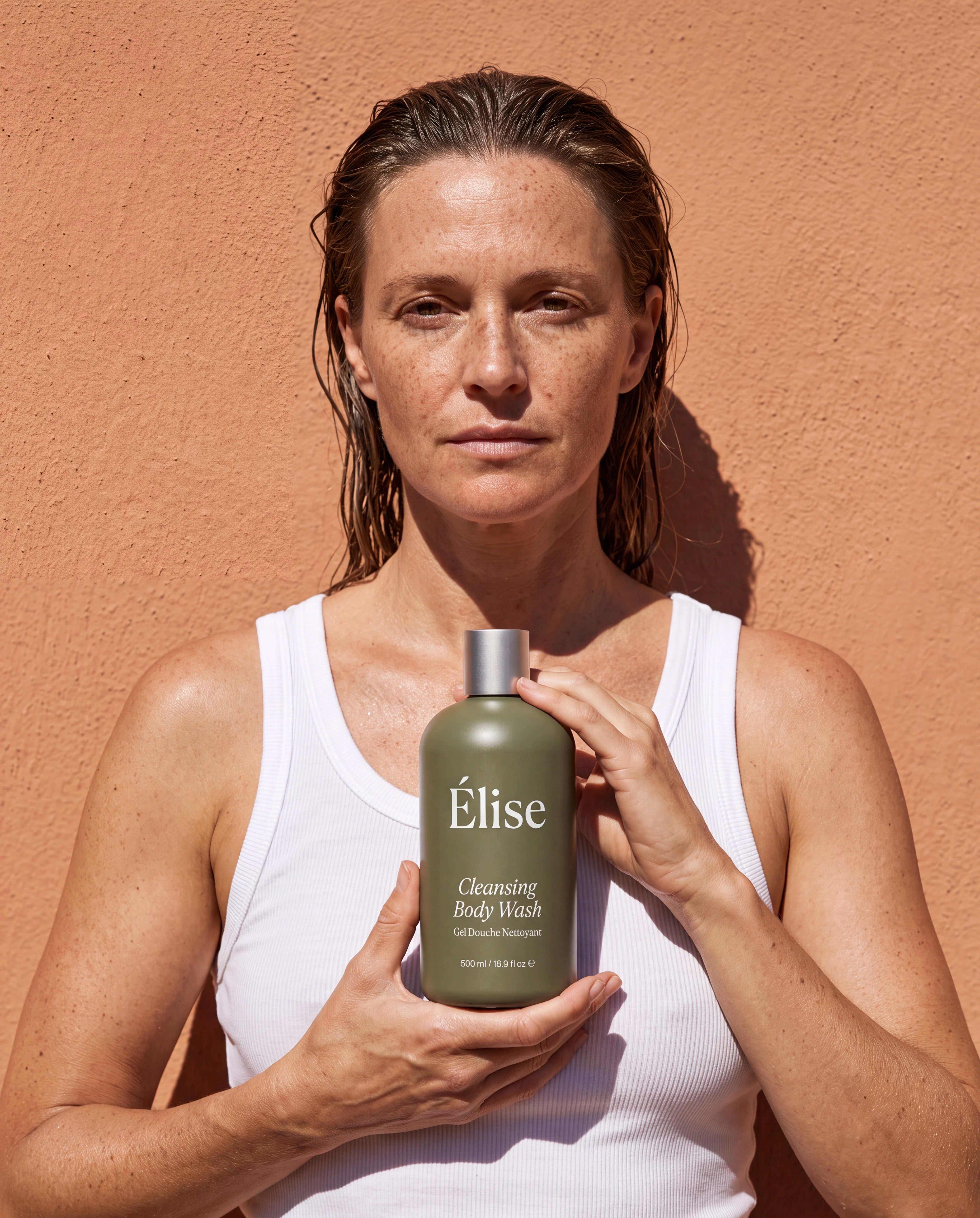A freckled woman holding one correctly scaled Elise bottle against sunlit terracotta