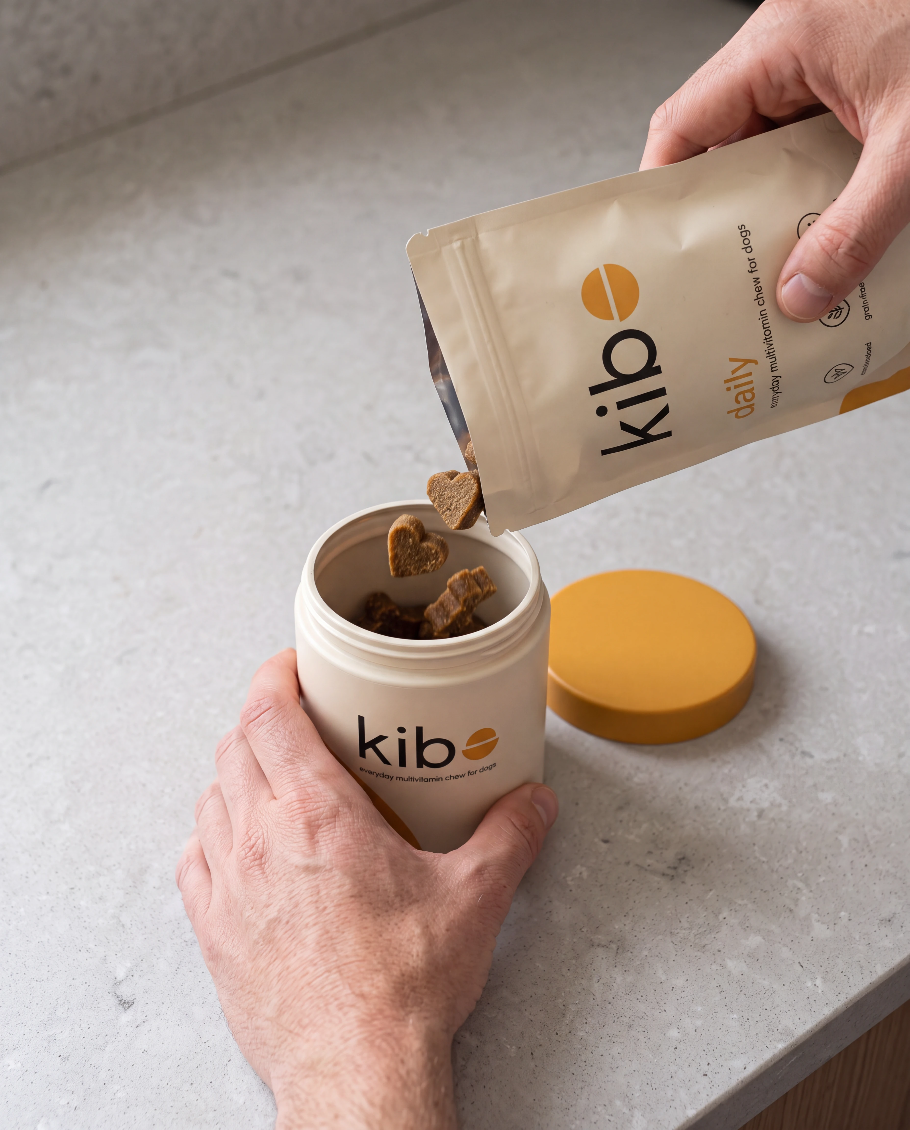Hands refilling a palm-sized Kibo jar from the daily pouch