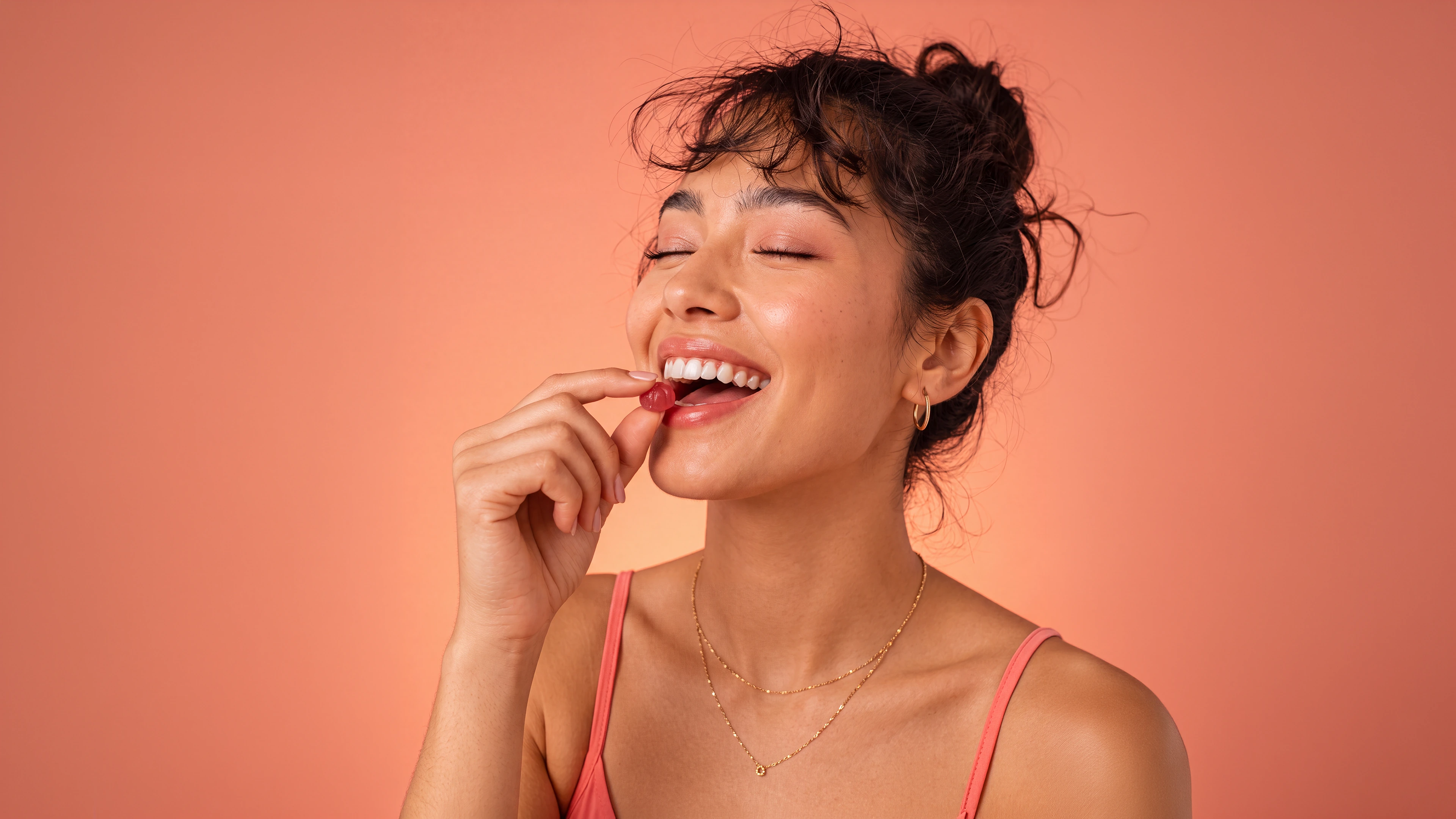 A woman smiling naturally as she brings one red Luma gummy toward her mouth
