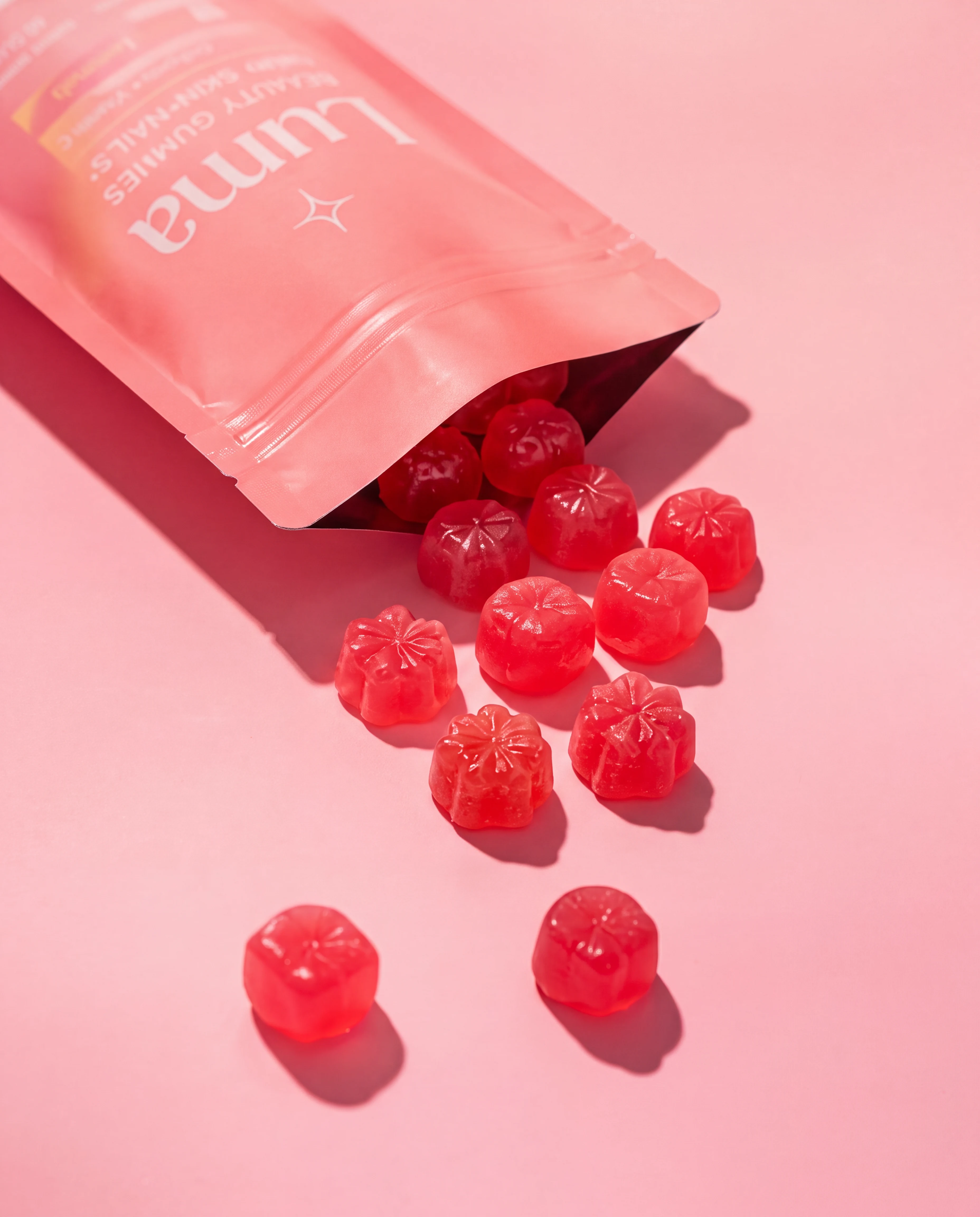 A coral Luma pouch spilling ruby gummies across a pink surface