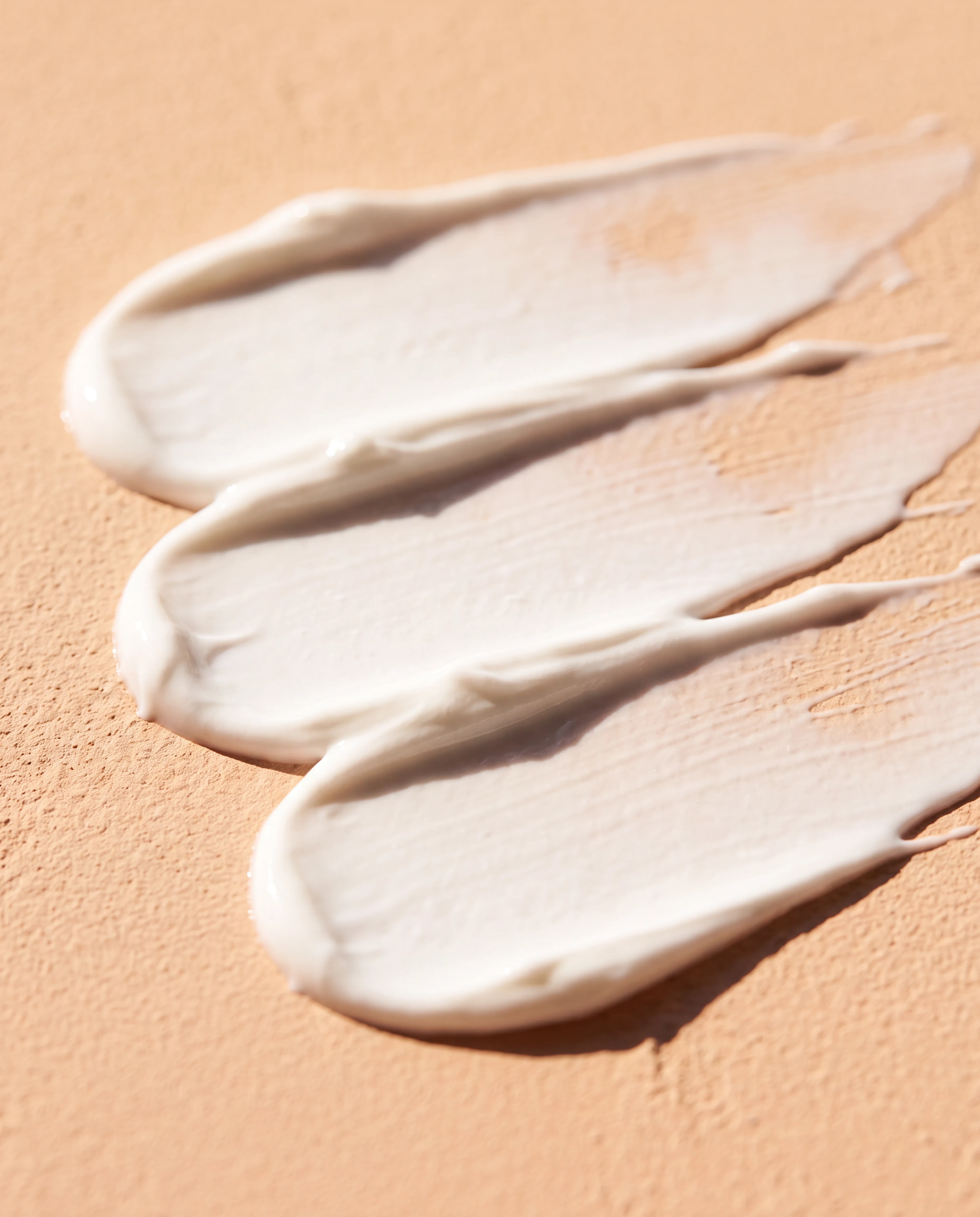 Tactile swipes of white mineral sunscreen across a peach-beige surface
