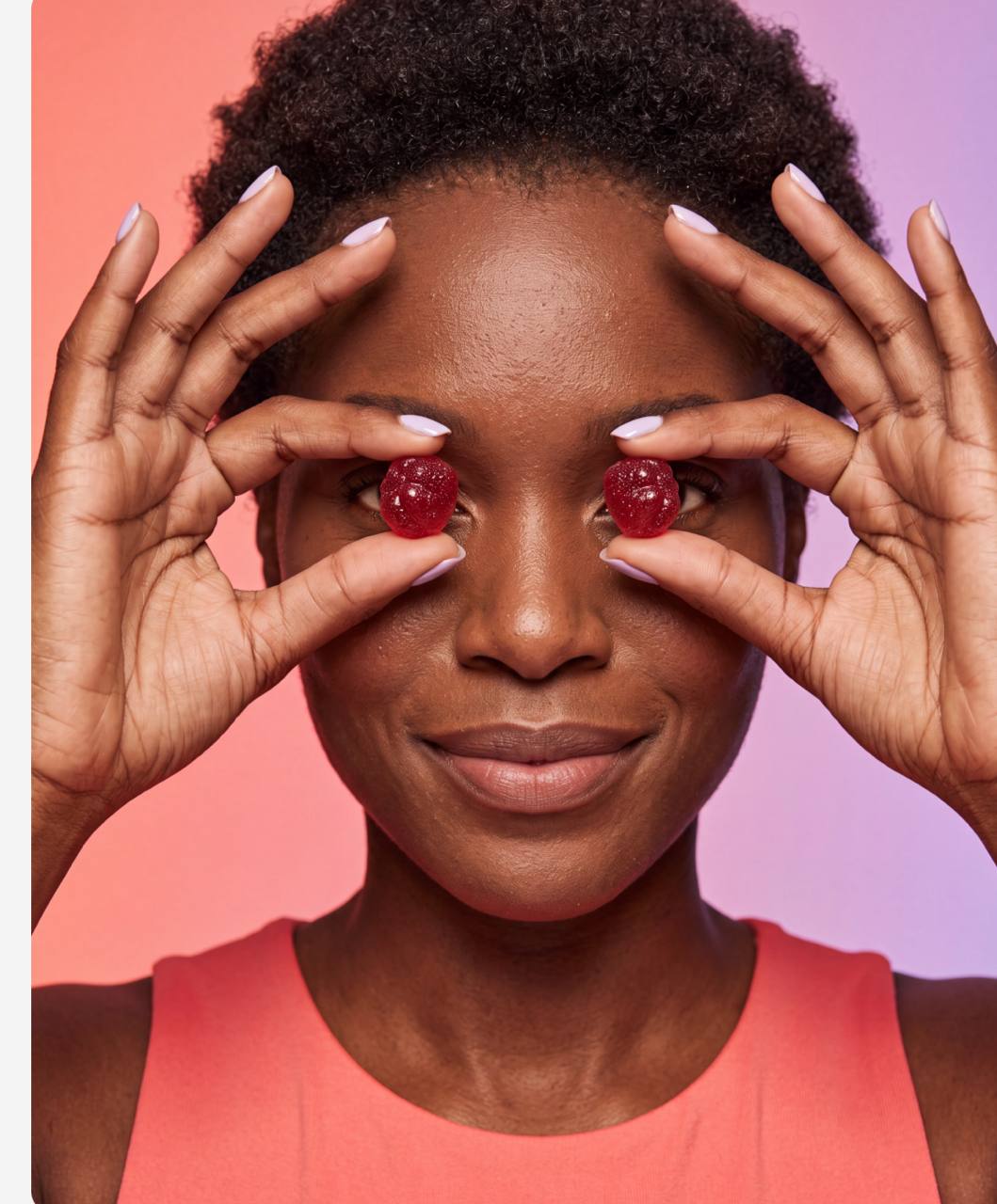 Woman holding two red gummies in front of her eyes against a coral and lavender background
